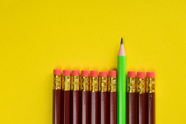 Business concept - lot of same pencils and one different pencil on yellow paper background. It's symbol of leadership, teamwork.