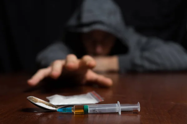 Addict at the table pulls his hand to the syringe with the dose — Stock Photo, Image