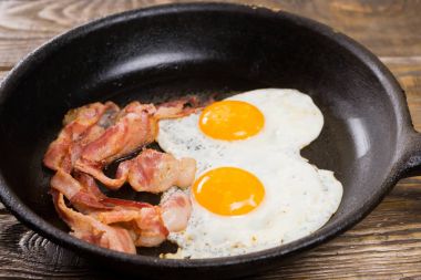 Pastırma ve yumurta. Tuzlu yumurta ve karabiber ile serpilir. İngiliz kahvaltısı. Izgara domuz pastırması, iki ahşap masa üzerinde tava üzerinde yumurta.