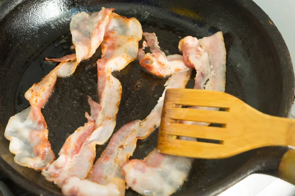 Pedaços de bacon são fritos em uma panela. Preparação do café da manhã . — Fotografia de Stock