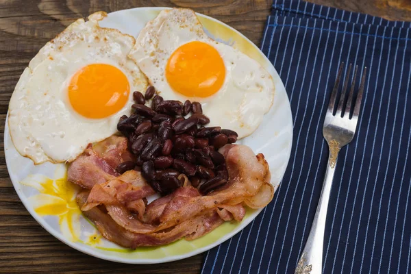 Teller mit Rührei, Speck und Bohnen auf einem rustikalen Holztisch. — Stockfoto