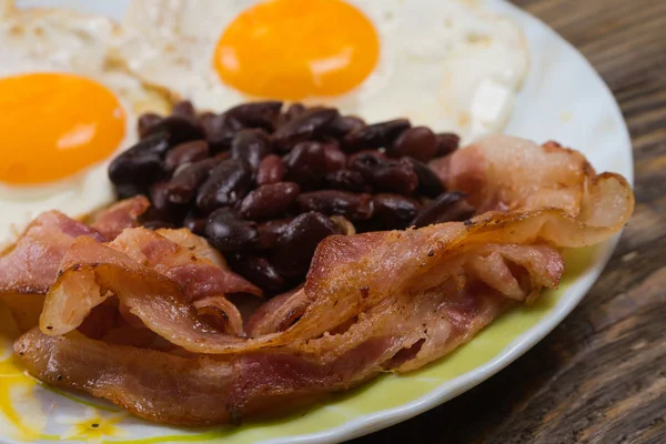 Prato com ovos mexidos, bacon e feijão em uma mesa rústica de madeira . — Fotografia de Stock