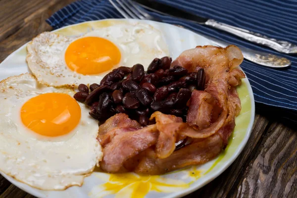 Piatto con uova strapazzate, pancetta e fagioli su un tavolo rustico in legno . — Foto Stock