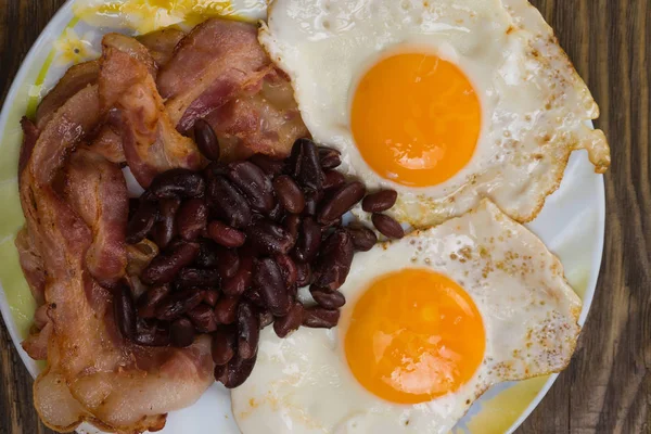 Prato com ovos mexidos, bacon e feijão em uma mesa rústica de madeira . — Fotografia de Stock