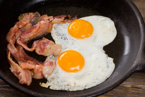 Speck und Ei. gesalzenes Ei und mit schwarzem Pfeffer bestreut. Englisches Frühstück. gegrillter Speck, zwei Eier auf Pfanne auf Holztisch. — Stockfoto