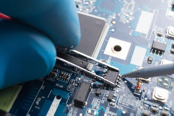 Mano con pinzas que sostienen el chip, soldador soldar en su lugar. Reparación informática. Macrofotografía. Copiar espacio . — Foto de Stock