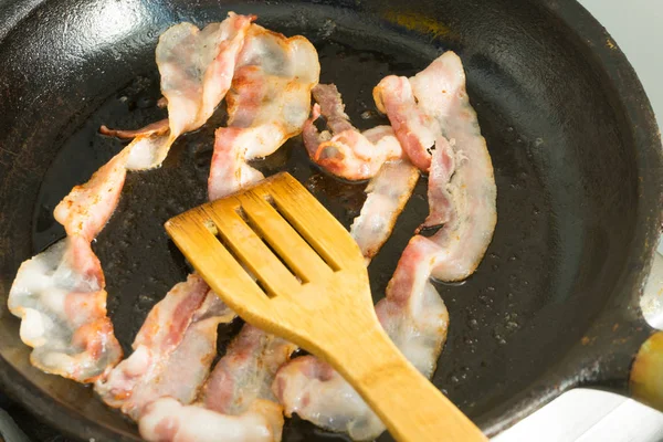 Pedaços de bacon são fritos em uma panela. Preparação do café da manhã . — Fotografia de Stock