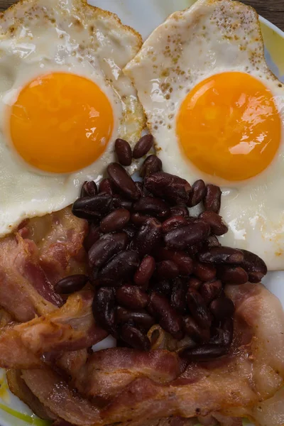 Prato com ovos mexidos, bacon e feijão em uma mesa rústica de madeira . — Fotografia de Stock