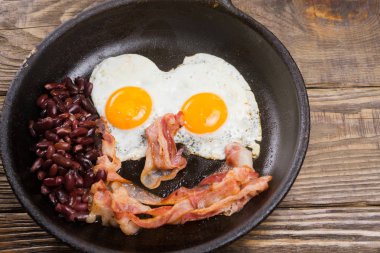 Sosis, yumurta ve fasulye. Tuzlu yumurta ve karabiber ile serpilir. İngiliz kahvaltısı. Izgara sosis, iki yumurta ve fasulye ahşap masa üzerinde tavada. kopya alanı