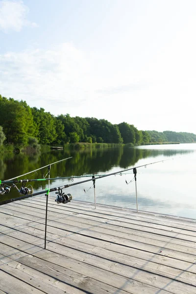 Karpfenangeln auf dem schönen blauen See mit Karpfenruten und Rutenschoten am Sommermorgen. Angeln von der Holzplattform. — Stockfoto