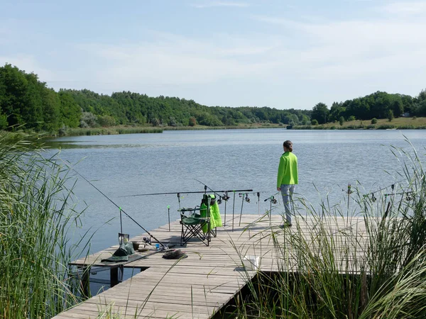 Girl carp fishing on beautiful blue lake with carp rods and rod pods in the summer morning. Fishing from the wooden platform.