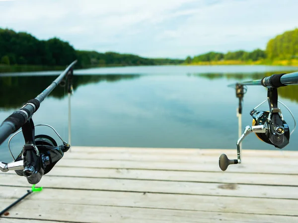 Karpfenangeln auf dem schönen blauen See mit Karpfenruten und Rutenschoten am Sommermorgen. Angeln von der Holzplattform. — Stockfoto