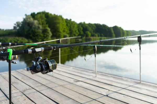 Karpfenangeln auf dem schönen blauen See mit Karpfenruten und Rutenschoten am Sommermorgen. Angeln von der Holzplattform. — Stockfoto