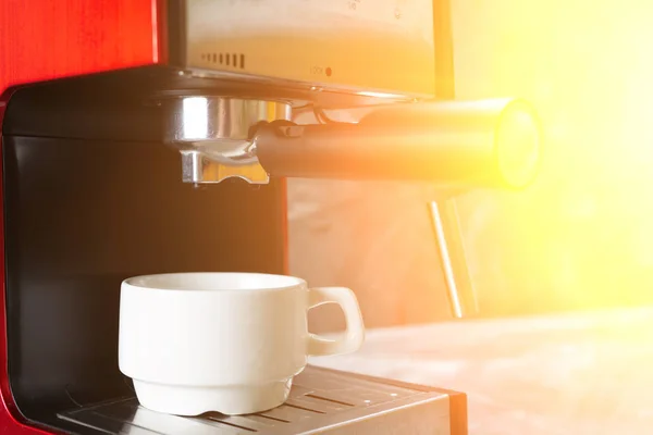 Copa blanca de pie en la rejilla de la máquina de café. Taza de espresso de cerámica blanca con cafetera sobre la mesa . — Foto de Stock