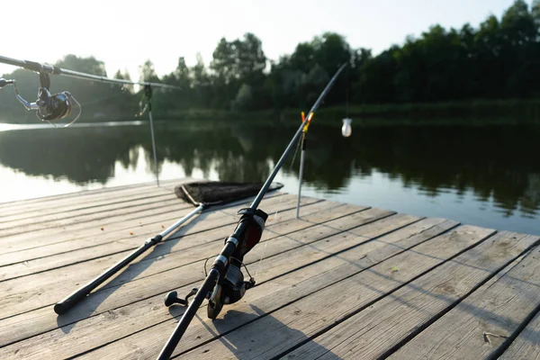 Karpfenangeln auf dem schönen blauen See mit Karpfenruten und Rutenschoten am Sommermorgen. Angeln von der Holzplattform. — Stockfoto