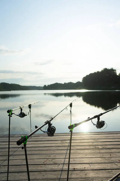 Karpfenangeln auf dem schönen blauen See mit Karpfenruten und Rutenschoten am Sommermorgen. Angeln von der Holzplattform. — Stockfoto