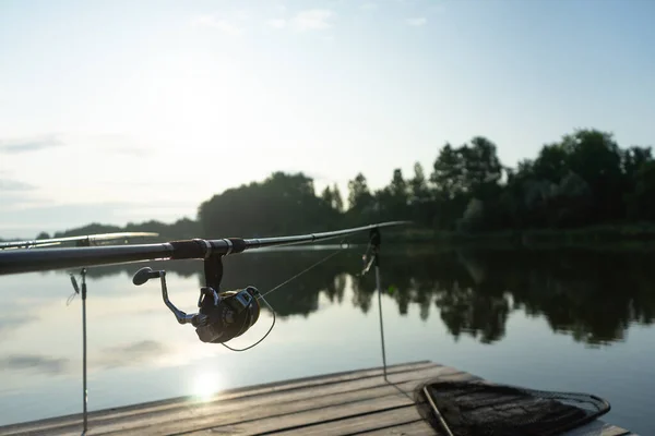 Karpfenangeln auf dem schönen blauen See mit Karpfenruten und Rutenschoten am Sommermorgen. Angeln von der Holzplattform. — Stockfoto