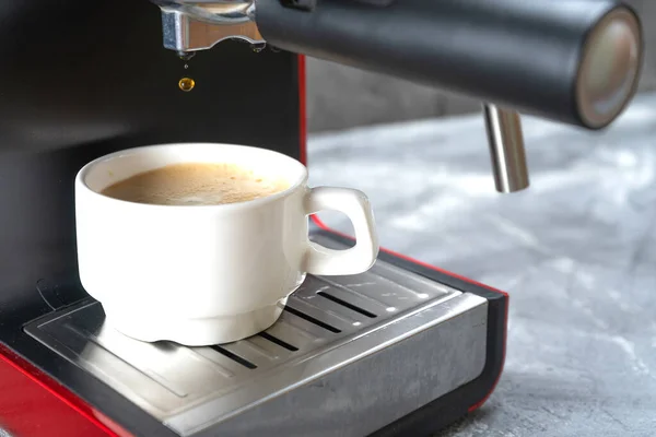 The last drop of coffee falls from the portafilter into the coffee Cup. Red coffee maker pouring hot espresso coffee in a white cup.