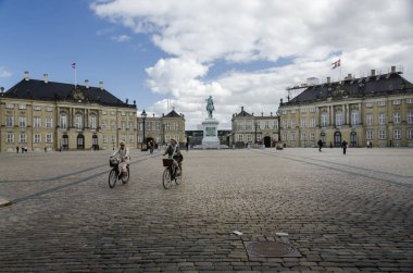 İki kadın bisikletle Saray Meydanı 'nda Amalienborg Sarayı' nı geçiyor. Arkalarında Kopenhag, Danimarka.