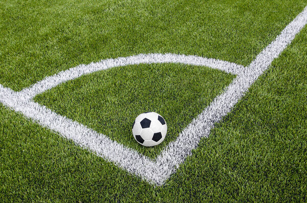 The soccer football in the corner on the artificial green grass field