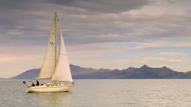 Ein Segelboot gleitet auf ruhigem Wasser in der Nähe von Bergen lizenzfreies Stockvideo