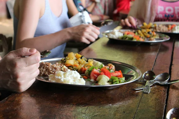 Közös vegetáriánus ebéd. Lányok eszik egy fából készült asztal fém edények. — Stock Fotó