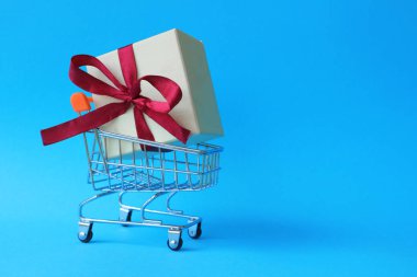 Şerit metin için yer ile mavi bir arka plan üzerinde bir alışveriş arabası ile kutu. Bir hediye satın.