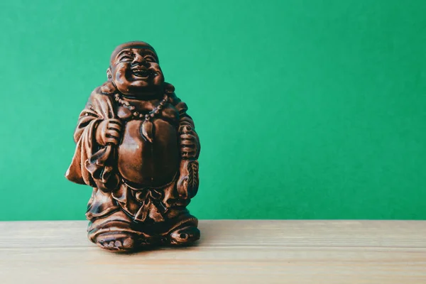 Hotei or the laughing Buddha is a Netsuke sculpture on a green background.