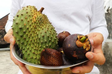 Beyazlı genç bir adam tropikal meyveli metal bir kase tutuyor: Annona muricata, yılan meyvesi ya da Allah, Mangosteen.