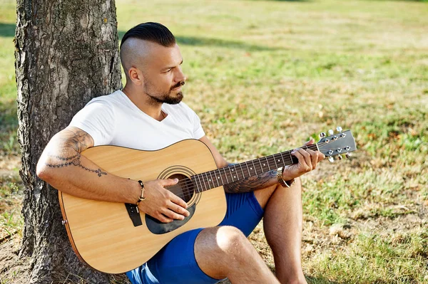 Красивый человек, поющий на гитаре в летнем парке — стоковое фото