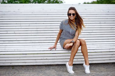 Güneş gözlüklü, bankta oturan güzel bir kadının moda portresi.