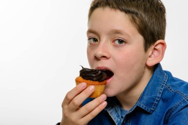 Genç çocuk kot gömlek eatng çikolatalı kek, beyaz izole arka planda. Yakın çekim.