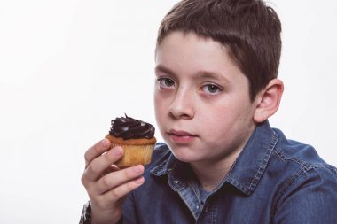 Genç çocuk kot gömlek beyaz izole zemin üzerine çikolatalı kek yeme. Portre kadar kapatın.