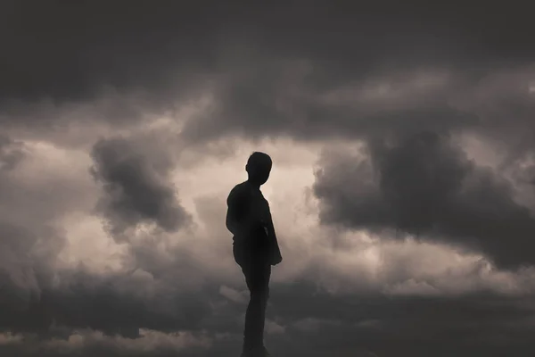 Boy silhouette on the background of clouds and darkness. A sense of loneliness, freedom, despair or helplessness. Vivid and strong vignetting effect. — Stock Photo, Image