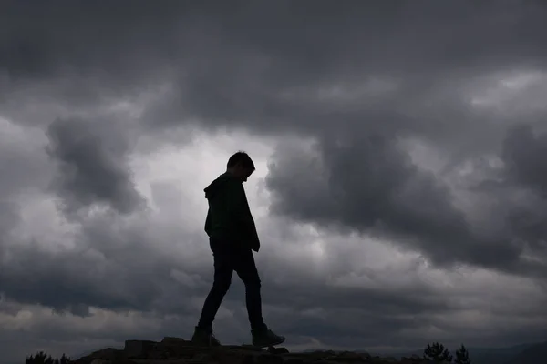 Boy silhouette on the background of clouds and darkness. A sense of loneliness, freedom, despair or helplessness. Vivid and strong vignetting effect. — Stock Photo, Image