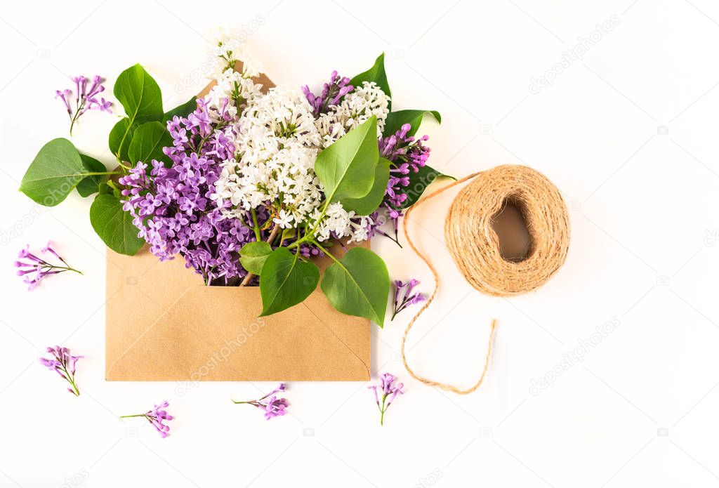 Close up of opened craft paper envelope filled with spring blossom purple lilac flowers laying on white background. Top view. Concept of love, gratitude and proposal.