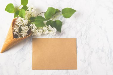 Çiçek kompozisyon. Leylak beyaz mermer zemin üzerinde gözleme koni ve zanaat zarf içinde. Yat, görünümü, kopya alanı top. Öneri, cazibe, Şükran, şefkat ve sevgi kavramı.