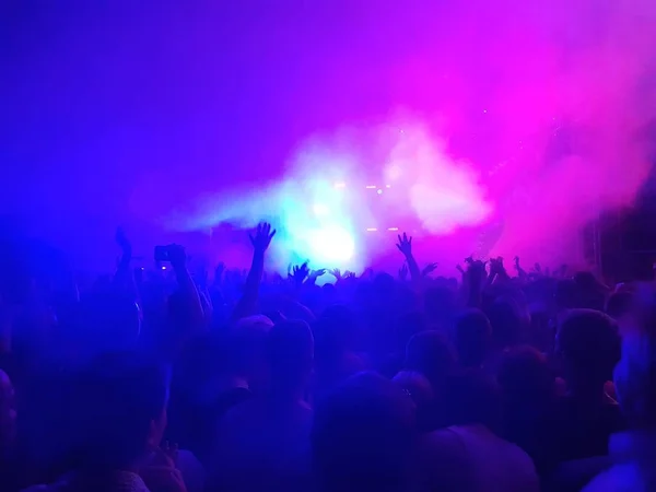 A crowd with their hands up in the air under the scene in Blue and purple smoke