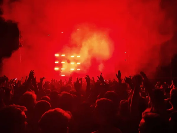 Una multitud con las manos en alto bajo la escena con humo rojo — Foto de Stock