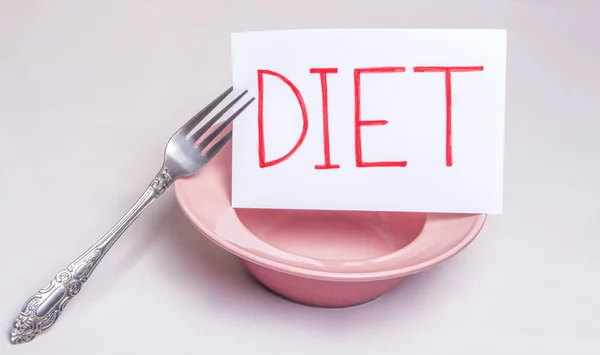 Η λέξη δίαιτα είναι γραμμένο σε ένα λευκό φύλλο που βρίσκεται σε ένα άδειο πιάτο με ένα πιρούνι τραπέζι — Φωτογραφία Αρχείου