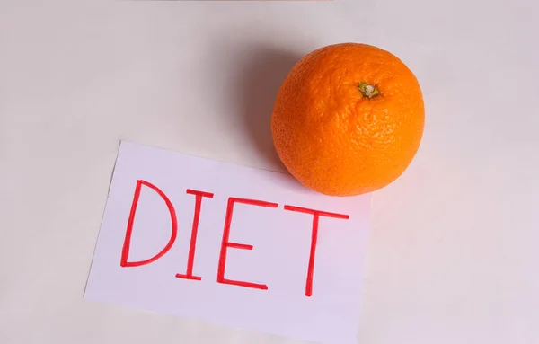 Слово дієта написано на білому аркуші з апельсином на світлому фоні — стокове фото
