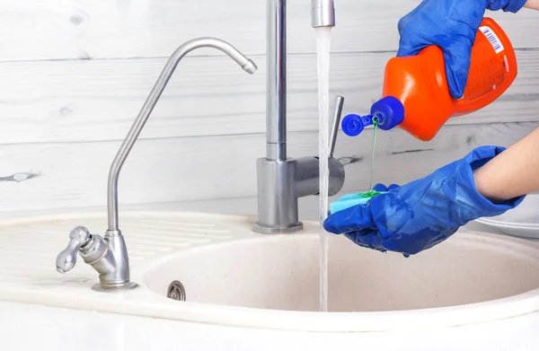 Η γυναίκα με τα μπλε γάντια ρίχνει απορρυπαντικό σε ένα σφουγγάρι για να πλύνει τα πιάτα. — Φωτογραφία Αρχείου