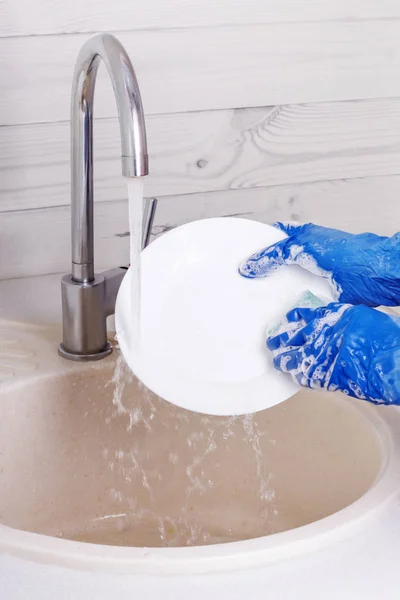 Γυναίκα με μπλε γάντια πλένει ένα πιάτο στην κουζίνα — Φωτογραφία Αρχείου