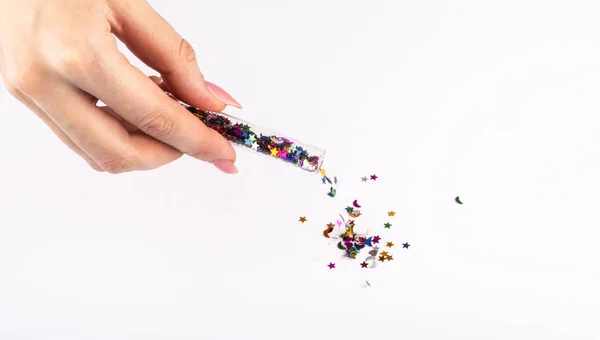 La fille saupoudre des paillettes colorées de différentes formes du bocal sur un fond blanc — Photo