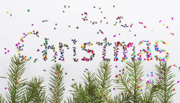 Fir branches and the word Christmas written in colored sequins of various shapes — ストック写真