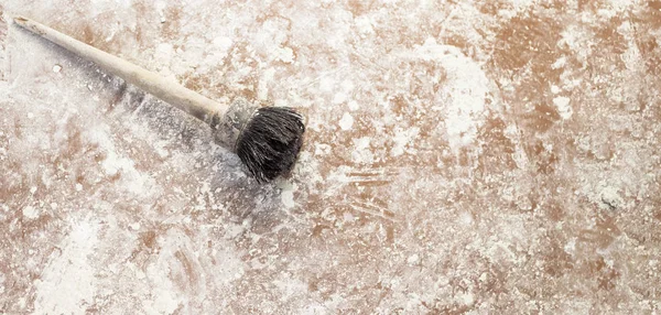 A big old paintbrush lying on the white-stained floor, copy space — стоковое фото