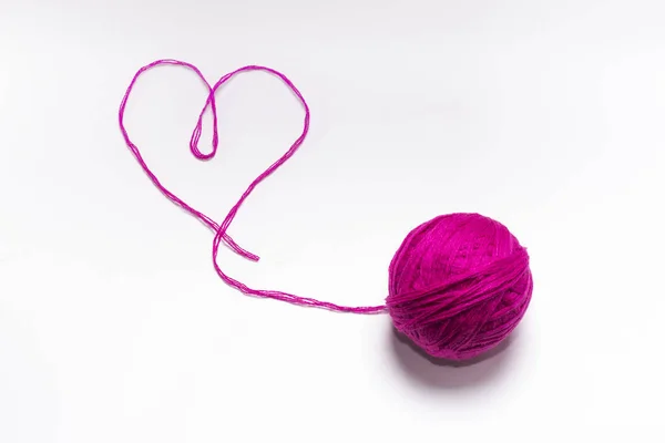 Novelo de lã rosa com um fio na forma de um coração em um fundo branco — Fotografia de Stock