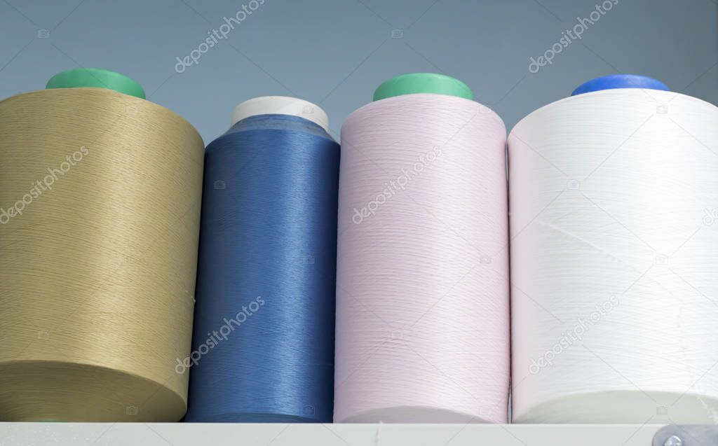 colored elastic threads wound on bobbins are on the shelf in the production