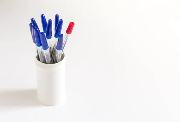 Ein roter Kugelschreiber unter vielen blauen Kugelschreibern auf weißem Hintergrund in einem weißen Glas — Stockfoto