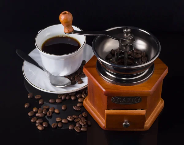 Кофемолка с чашкой кофе и кофе в зернах разбросаны между ними на черном фоне вид сверху — стоковое фото